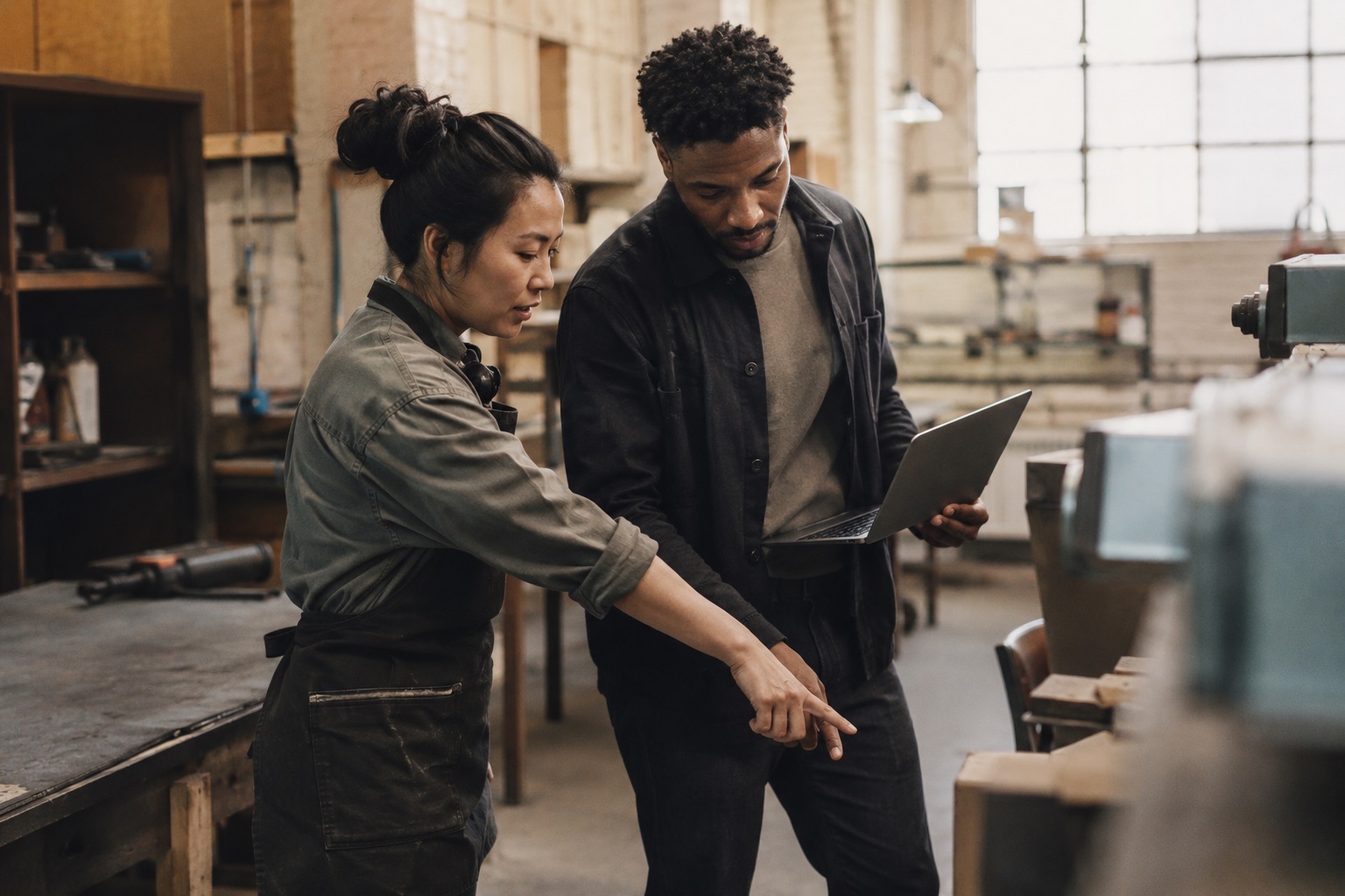 A workshop maker and a laptop-carrying technologist reviewing a machine together
